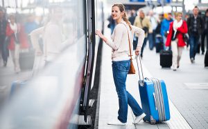 Frau wartet mit einem Koffer vor dem Zug