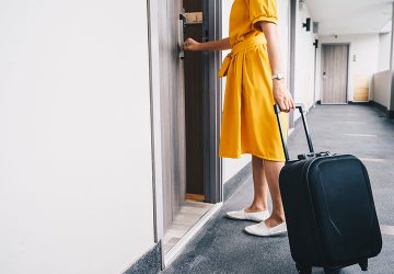 Frau mit Koffer sperrt Tür auf