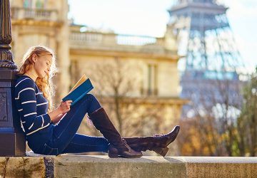 Frau ließt ein Buch, hinter ihr der Eiffelturm